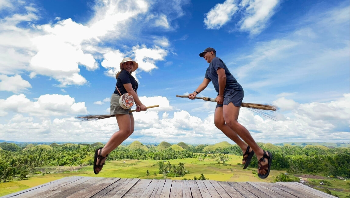 Tourists jumping with broomsticks at Chocolate Hills viewpoint in Bohol Philippines
