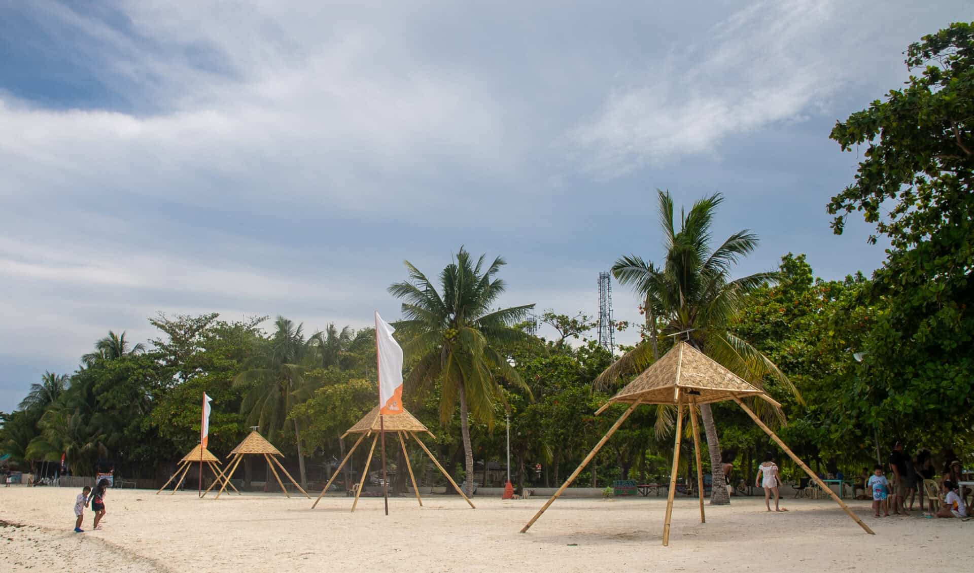 White sand beach with traditional bamboo cottages and coconut trees along Anda Beach in Bohol Island Geopark, Philippines.