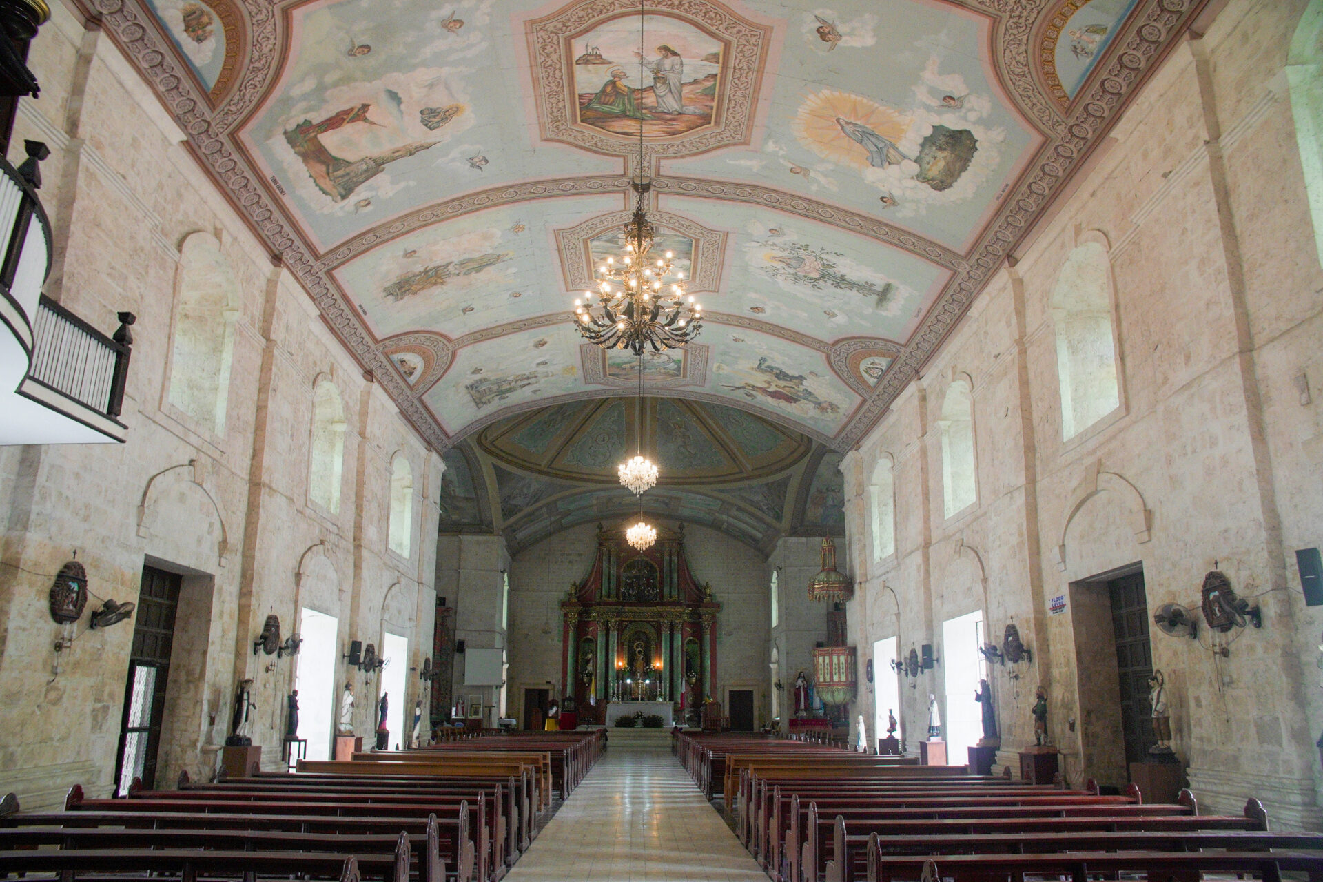 Interior of St. Peter the Apostle Parish in Loboc featuring painted ceiling murals, historic altar, and Spanish colonial architecture in Bohol, Philippines.