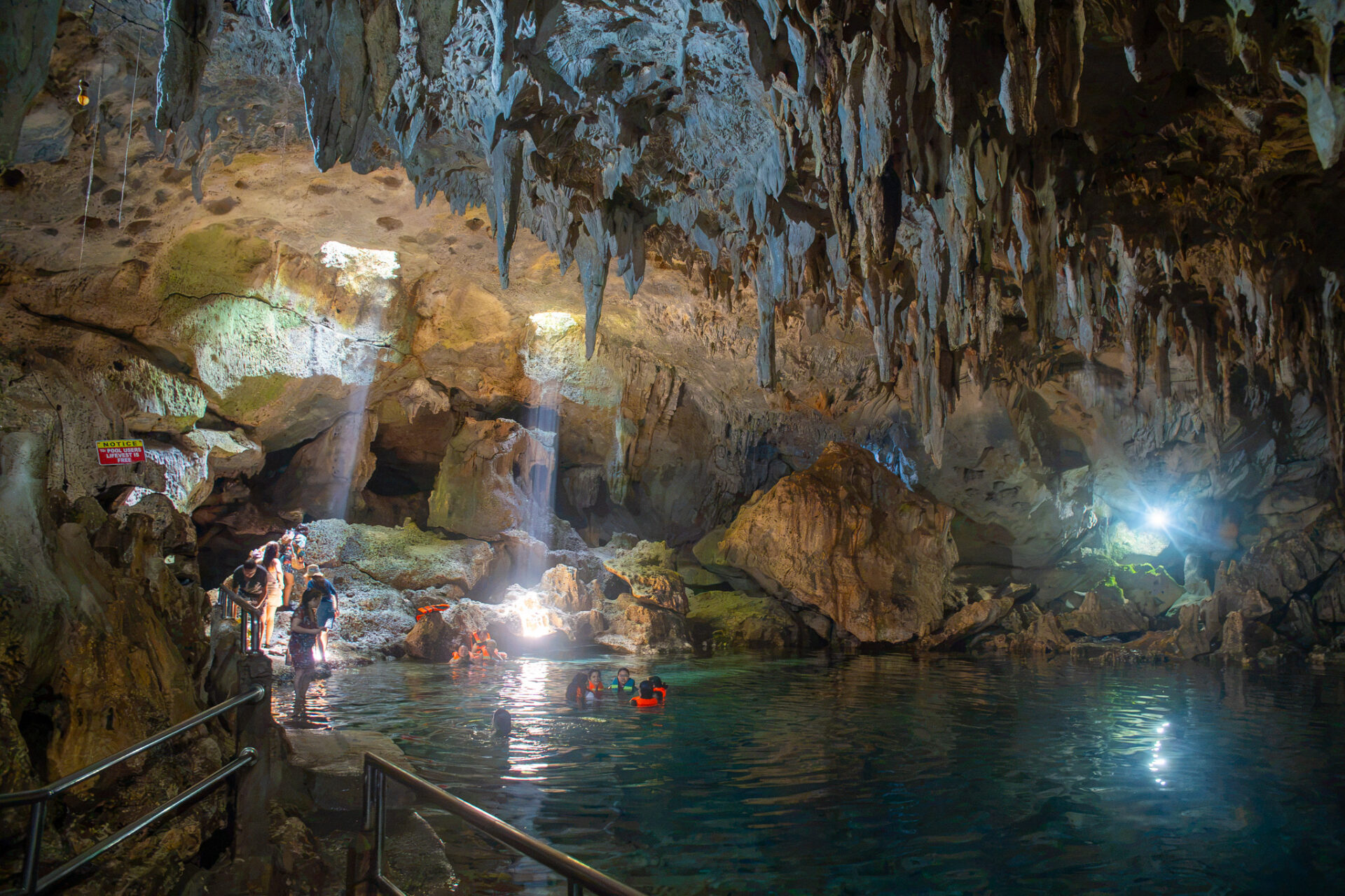 Visitors swimming inside Hinagdanan Cave in Panglao, Bohol, featuring crystal-clear water, limestone formations, and natural skylights.