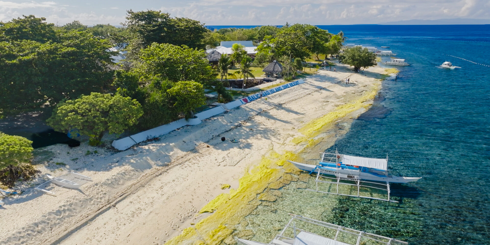 Aerial view of Balicasag Island featuring white sand beaches, crystal-clear waters, and traditional outrigger boats in Bohol Island Geopark.